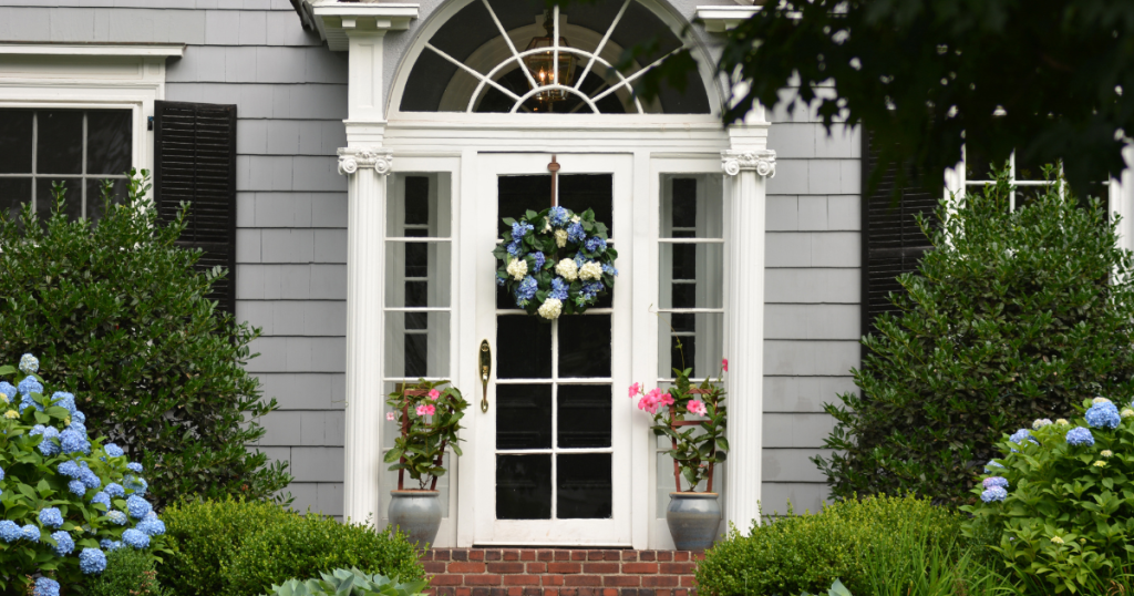 devanture maison grise avec une porte blanche vitrée, des arbustes et fleurs
