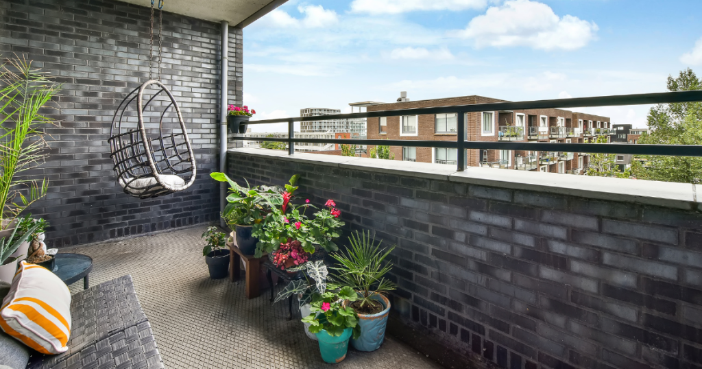 Petit balcon avec briques grises foncées, une chaise suspendue et des plantes feuillues